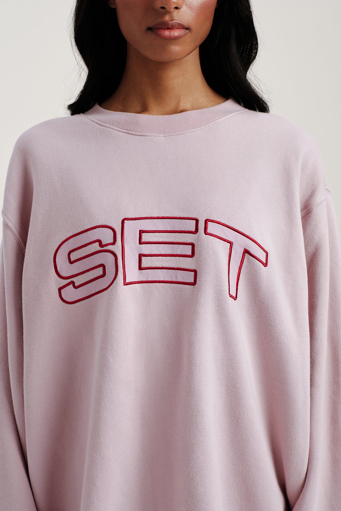 Person wearing a light pink sweatshirt with 'SET' printed in red.