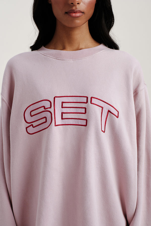 Person wearing a light pink sweatshirt with 'SET' printed in red.