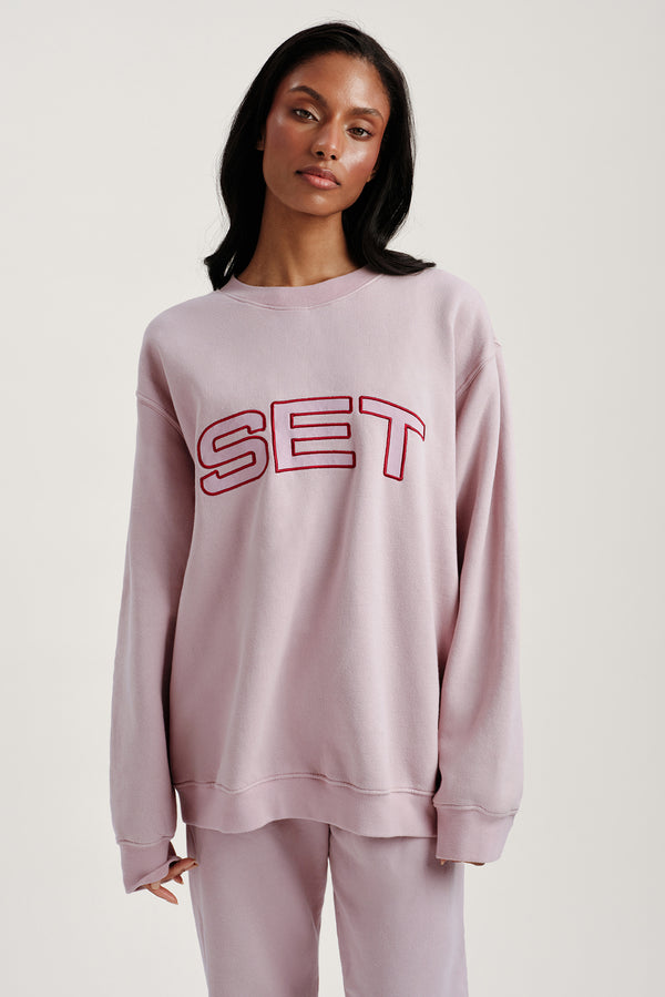 Woman wearing a pink sweatshirt with 'SET' printed on it against a white background