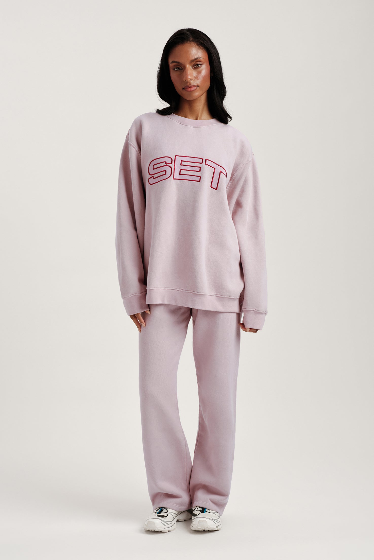 Person wearing a pink 'SET' sweatshirt and pants on a white background