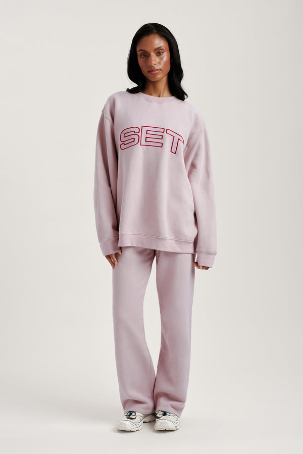 Person wearing a pink 'SET' sweatshirt and pants on a white background