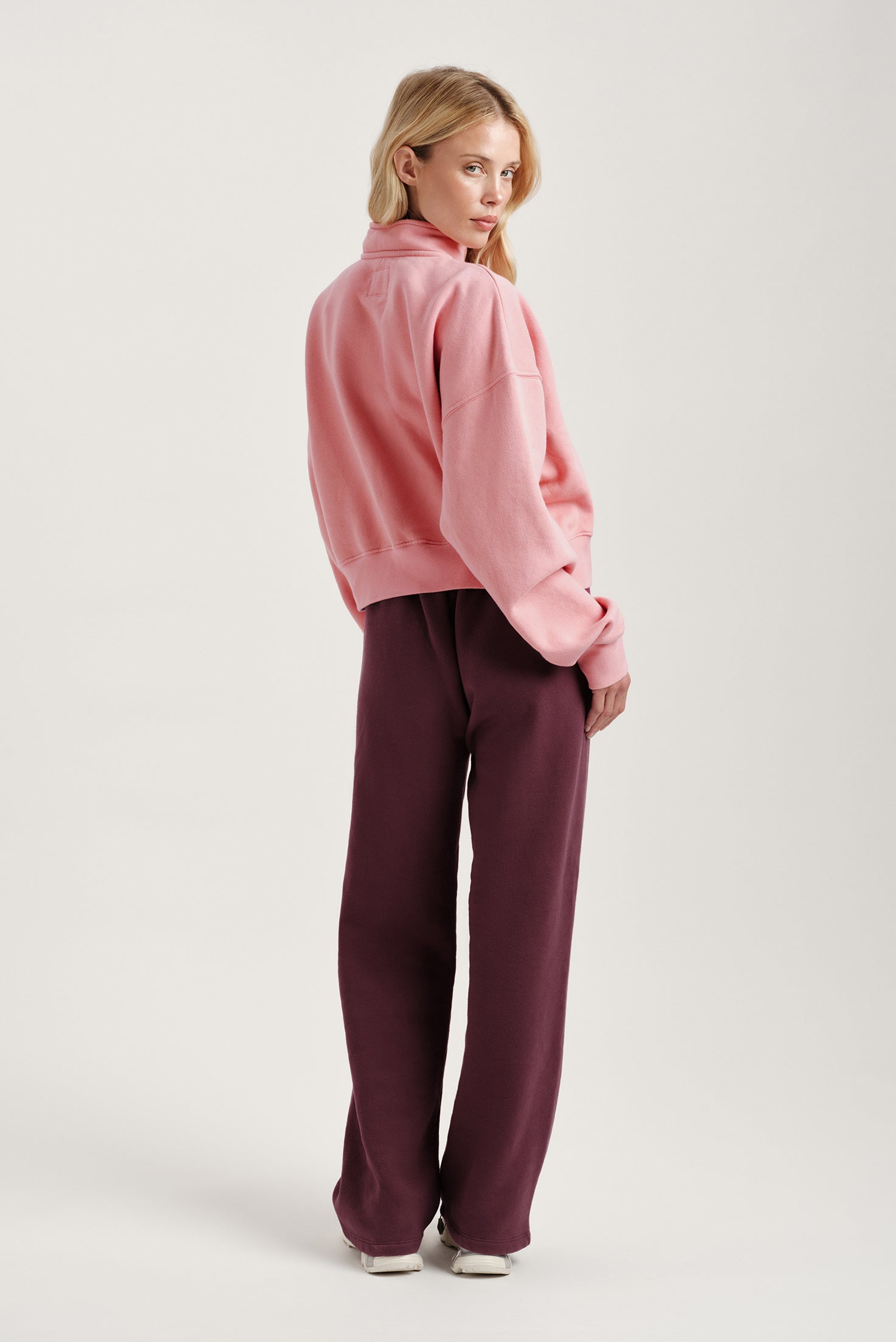 Woman wearing a pink fleece jacket and burgundy pants on a light gray background