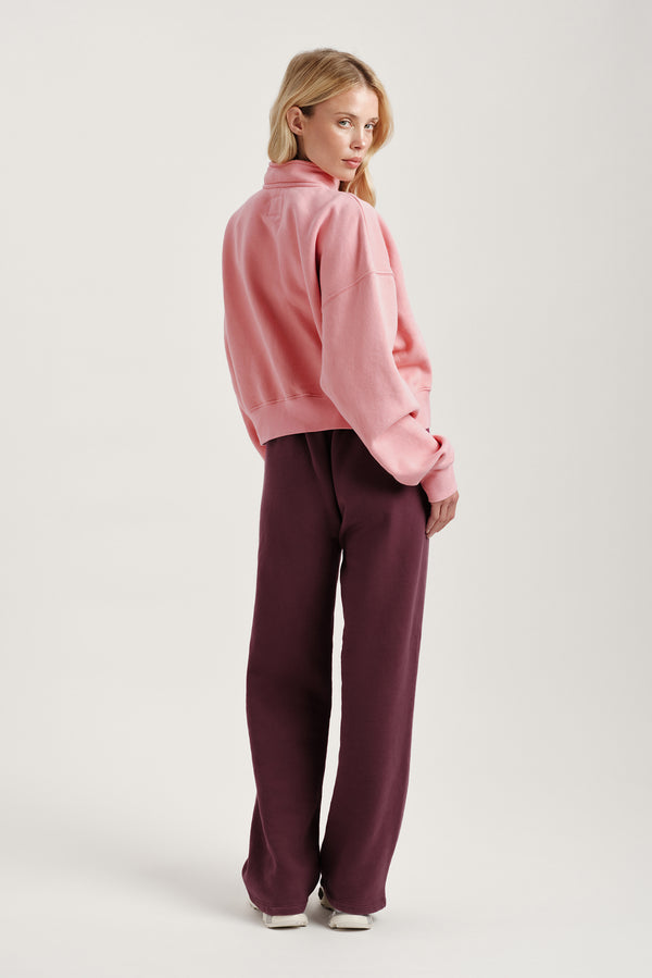 Woman wearing a pink fleece jacket and burgundy pants on a light gray background