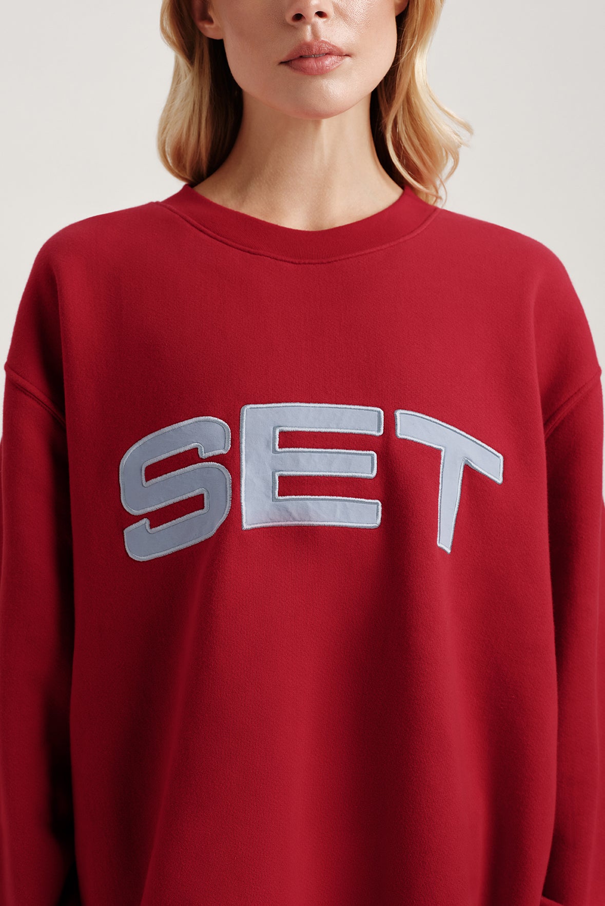 Red sweatshirt with 'SET' text worn by a person on a light background