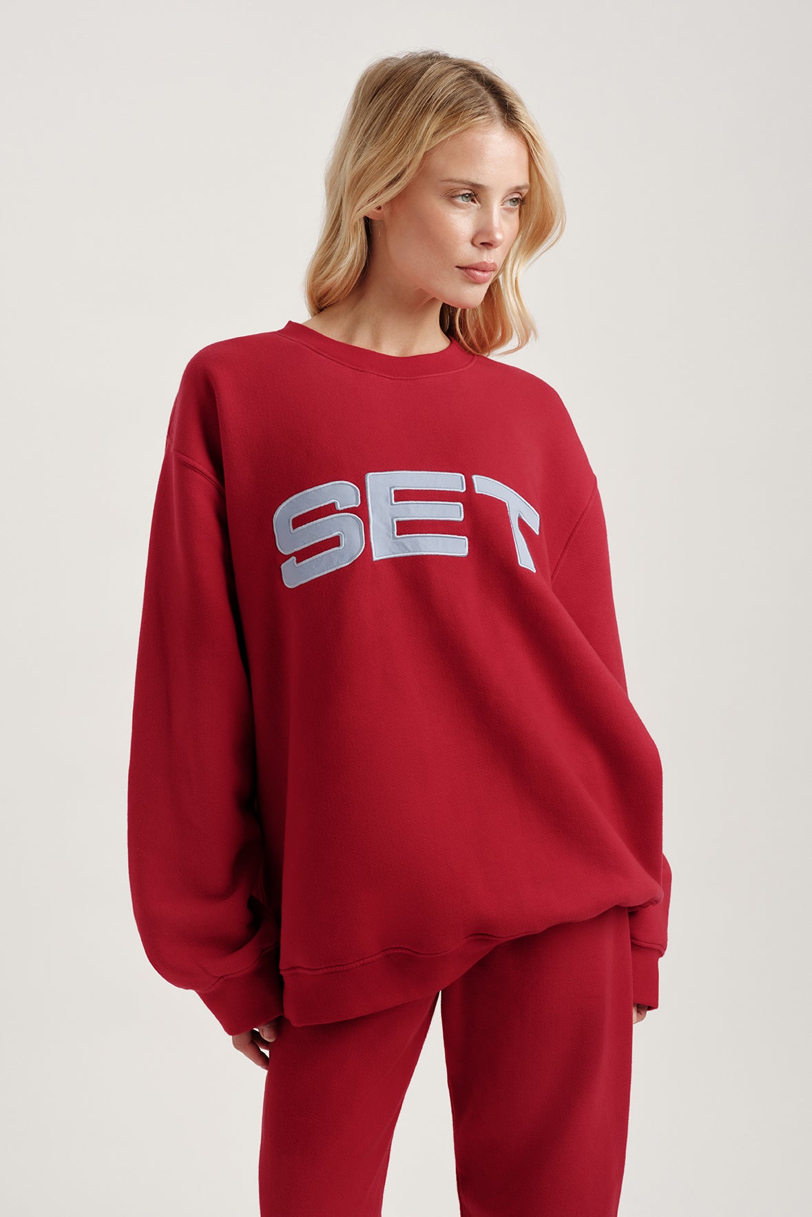 Person wearing a red sweatshirt with 'SET' text on a plain background
