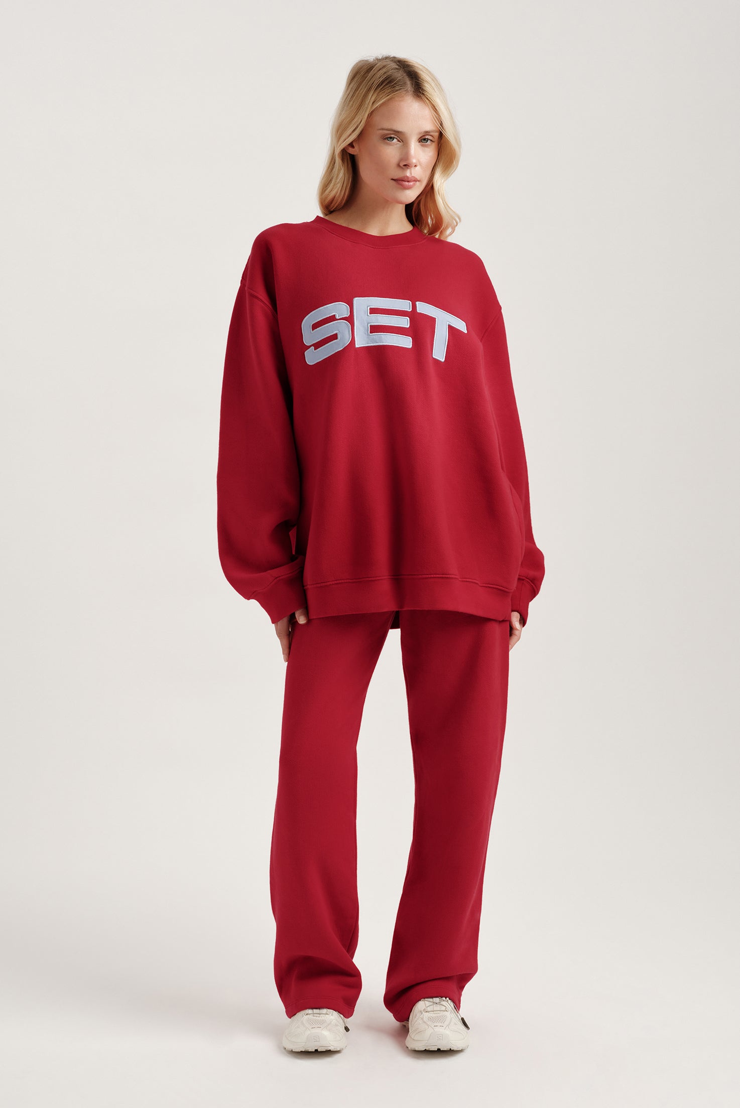 Person wearing a red 'SET' sweatshirt and pants on a white background