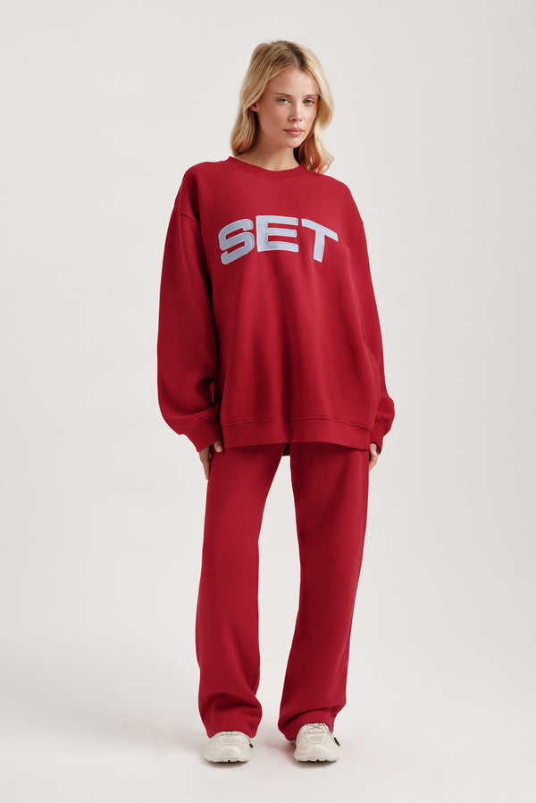 Person wearing a red 'SET' sweatshirt and pants on a white background