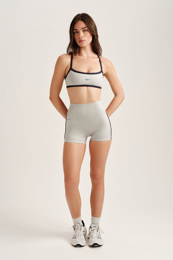 Woman wearing a sports bra and shorts on a plain background