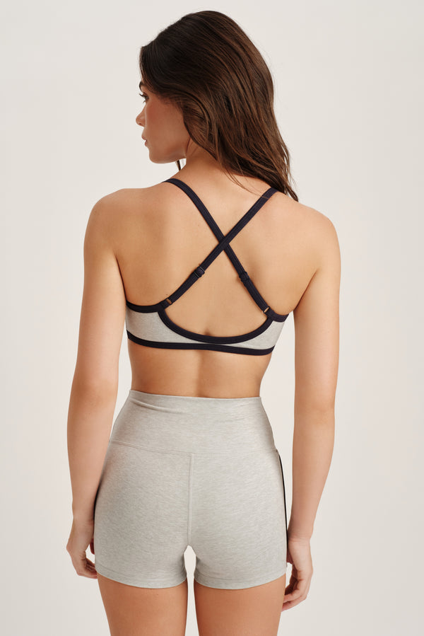 Woman wearing a navy and gray sports bra with criss-cross straps on a plain background