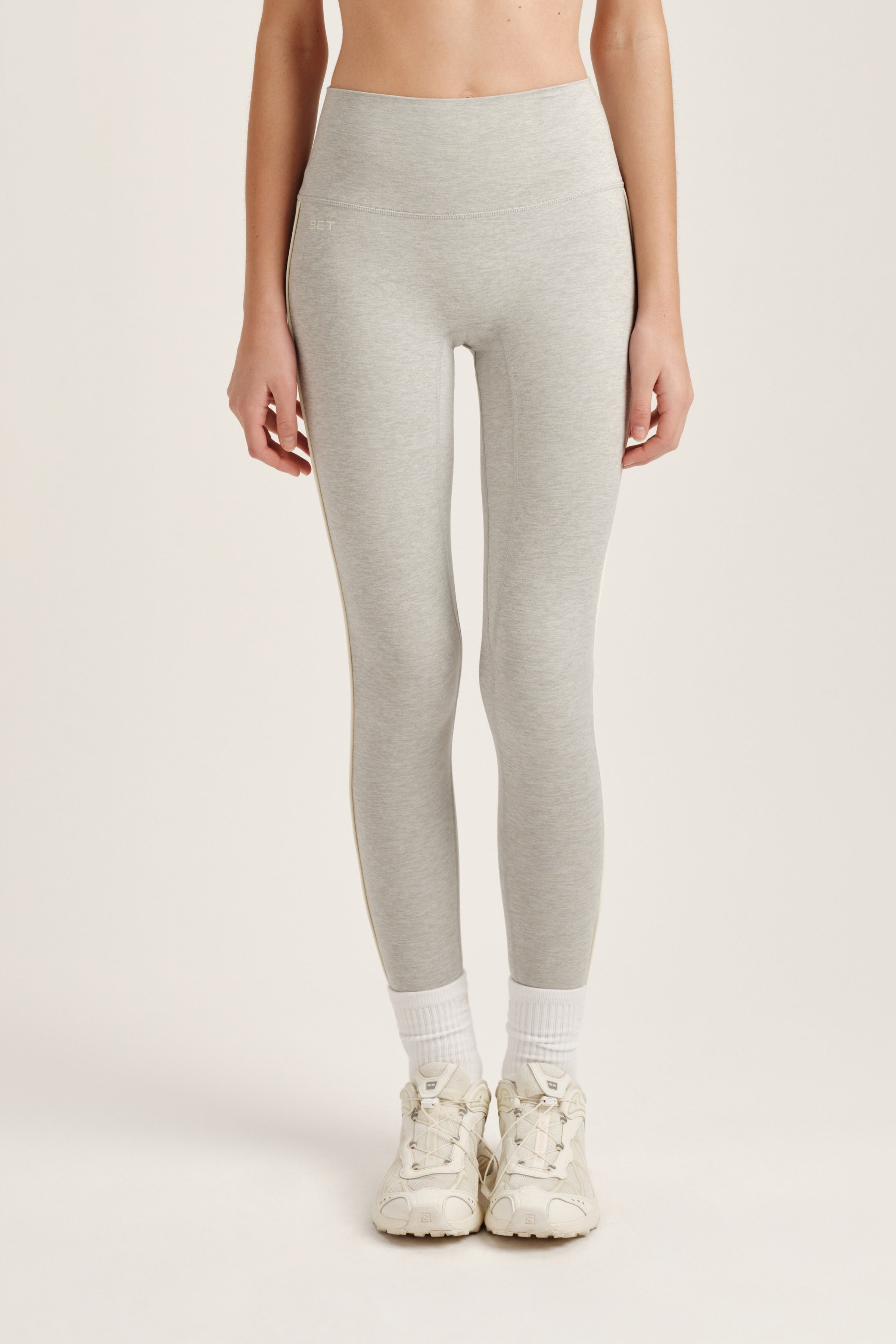 Person wearing light gray leggings and white sneakers on a plain background 