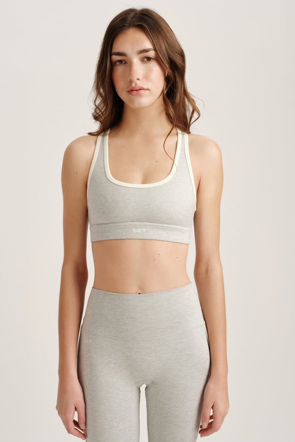 Woman wearing a gray sports bra and leggings on a plain  background 
