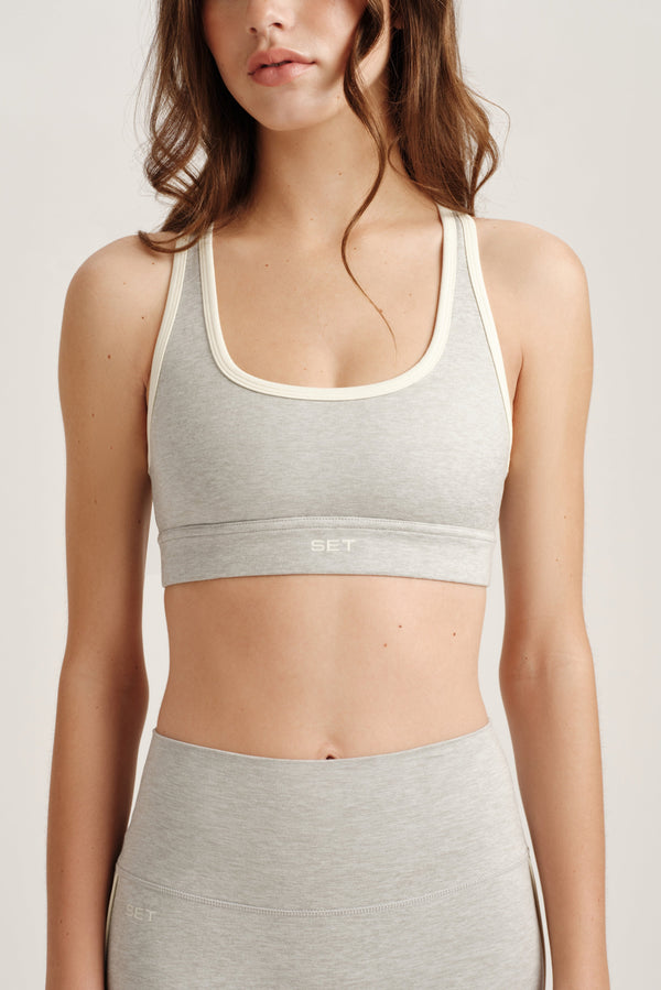 Woman wearing a gray sports bra and leggings on a plain background