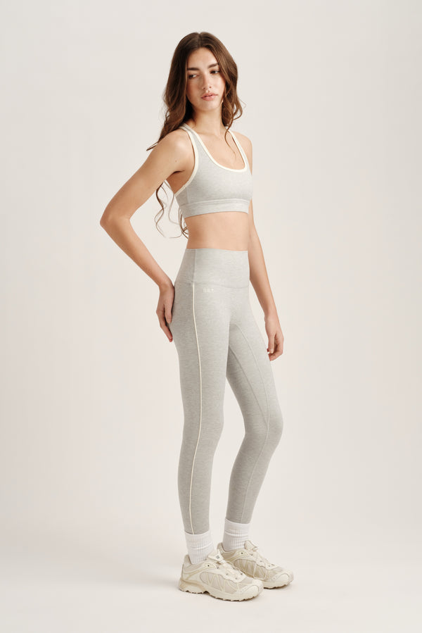 Woman wearing a light gray sports bra and leggings set on a white background