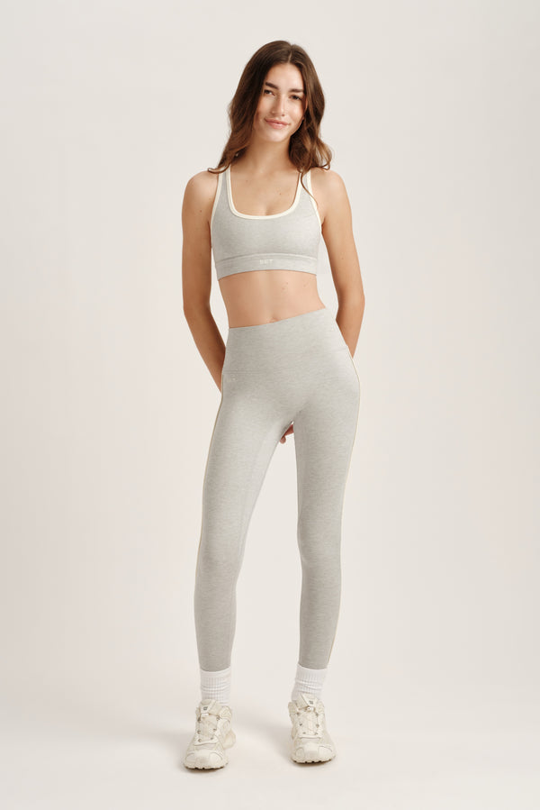 Woman wearing a light gray sports bra and leggings set on a white background