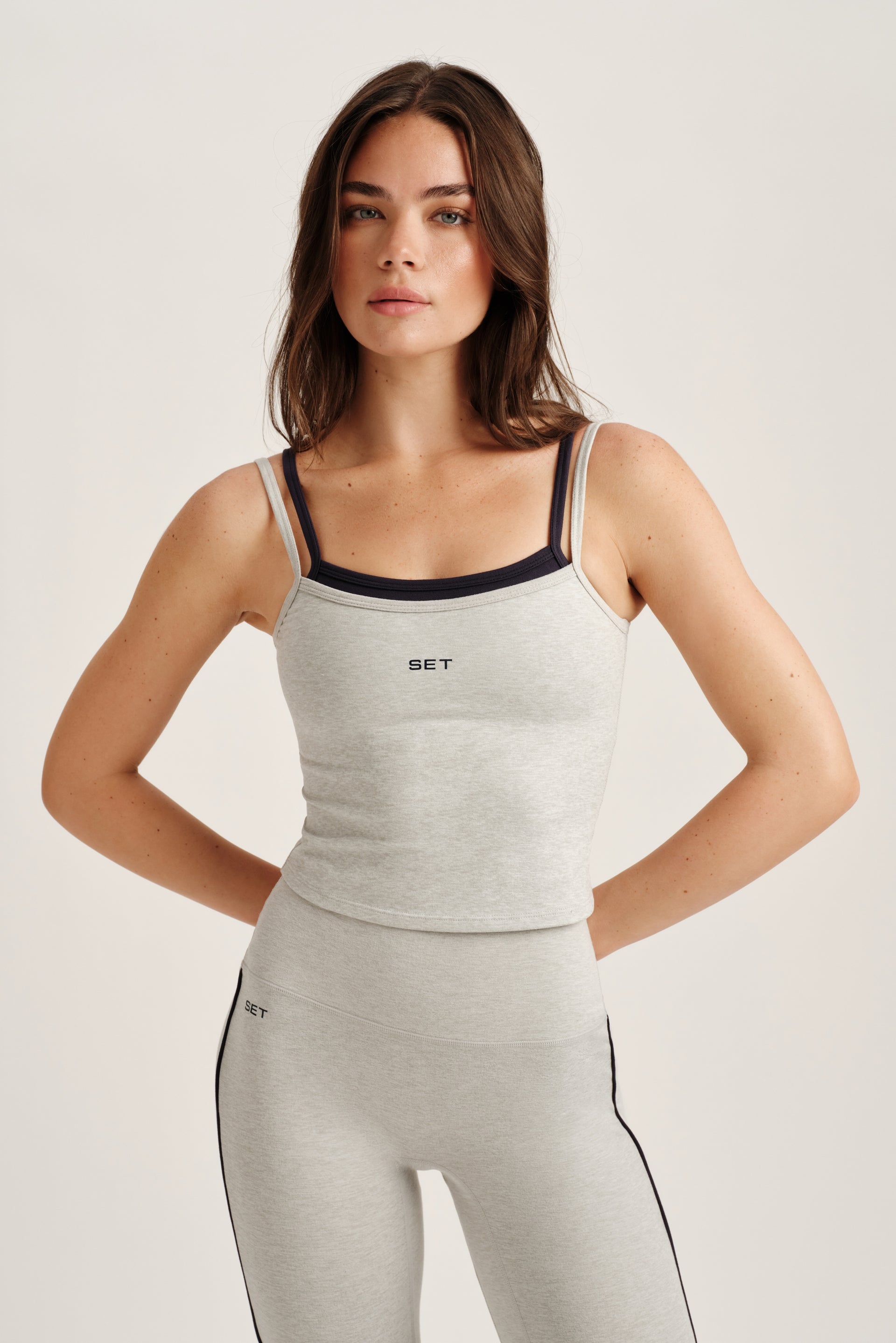 Woman wearing a gray tank top and leggings with a visible brand logo on a light background <model-info>Bella wears a size XS and is 5’7, 23” waist, 32AB bust.</model-info>