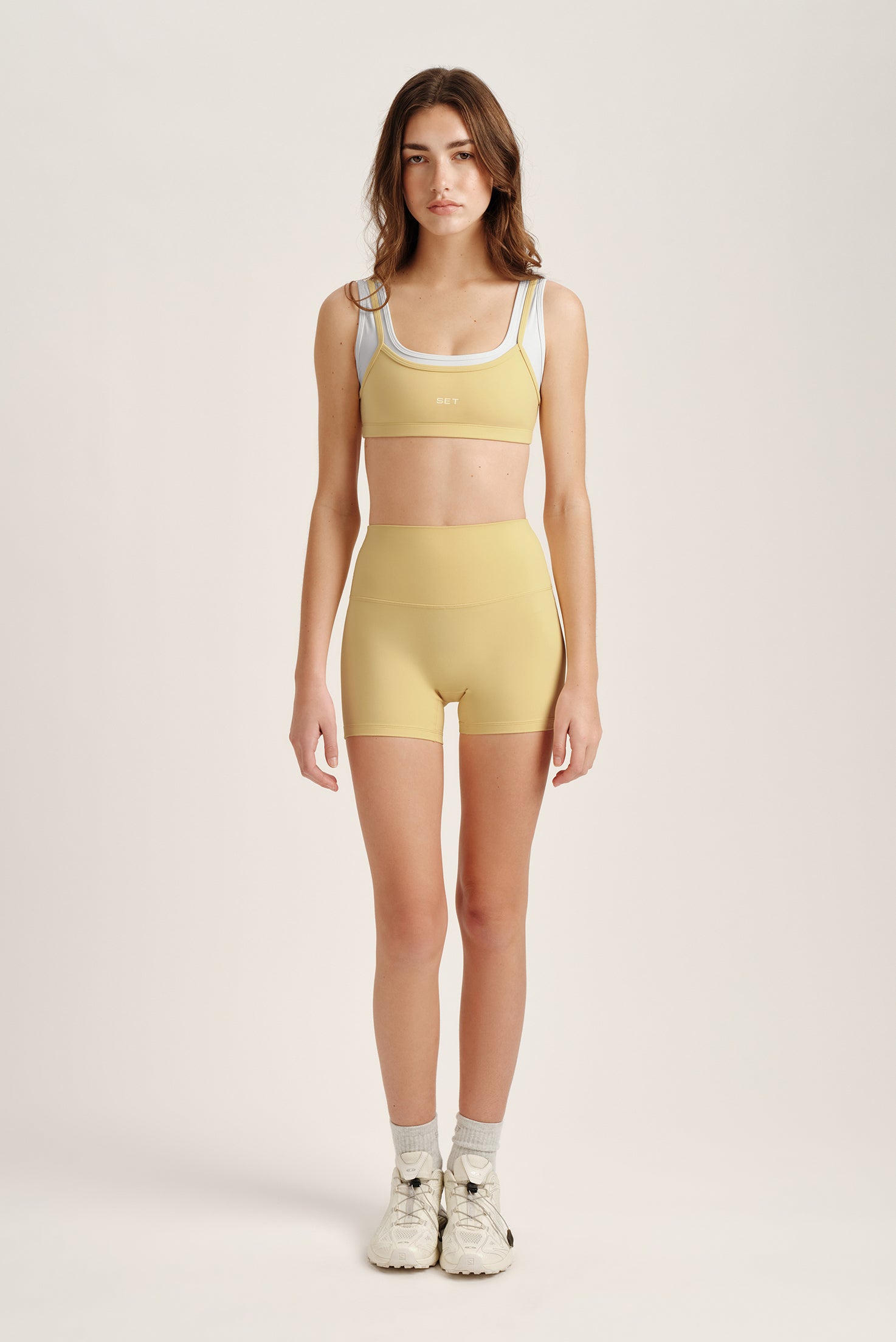 Woman wearing a yellow sports bra and shorts set on a plain background