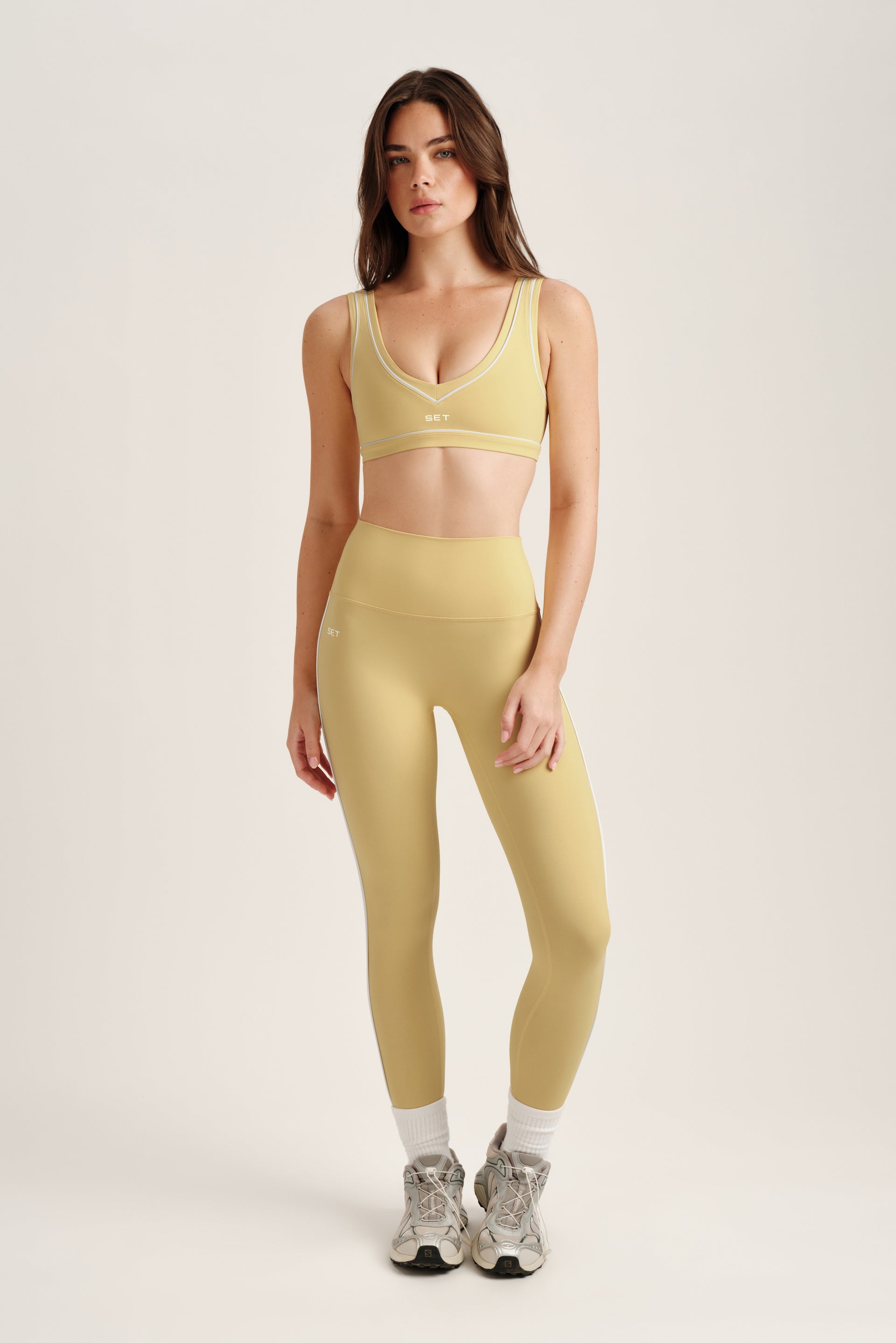 Woman wearing a yellow sports bra and leggings set on a white background