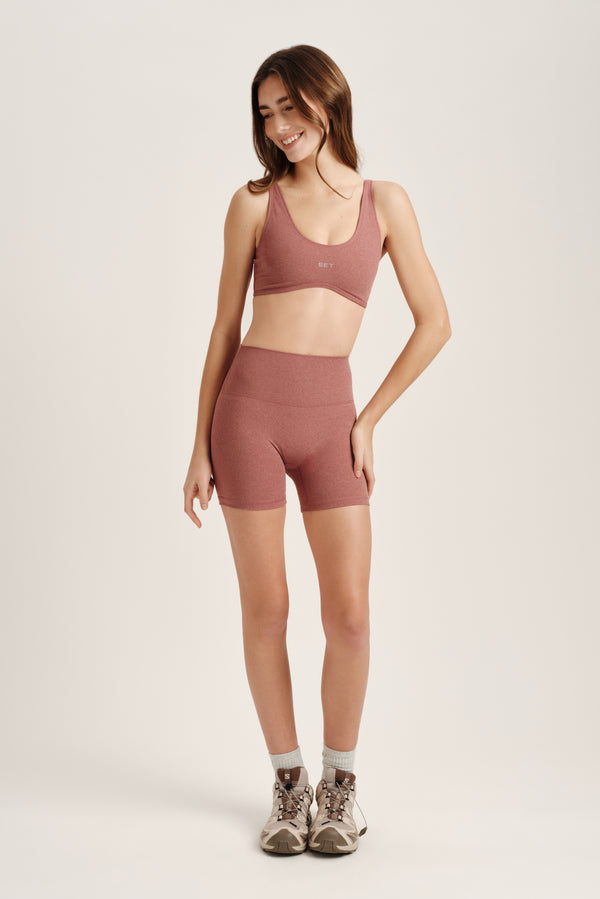 Woman wearing a pink sports bra and shorts set on a light background