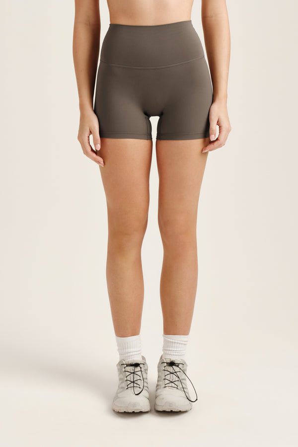 Person wearing olive green high-waisted shorts on a beige background 