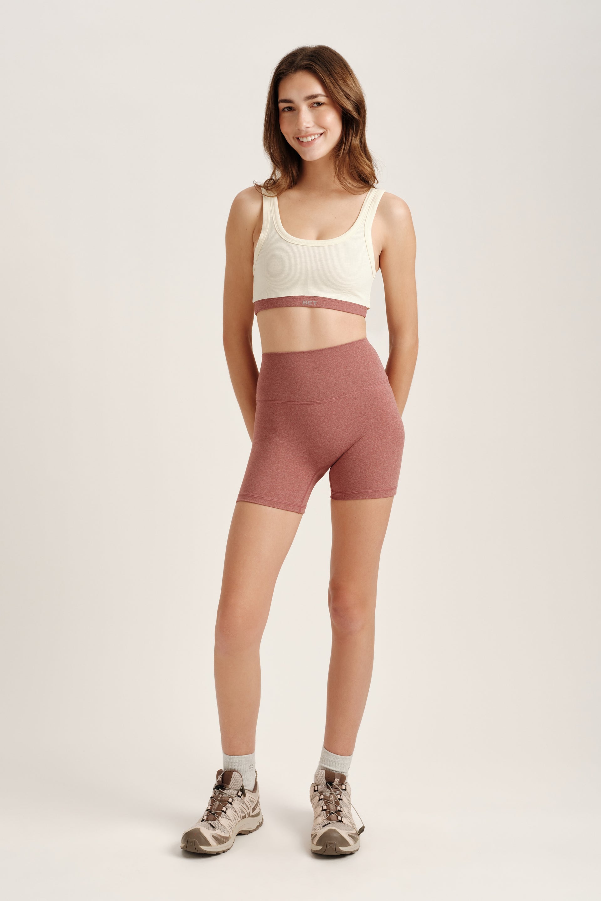 Woman wearing a white tank top and pink shorts on a plain background