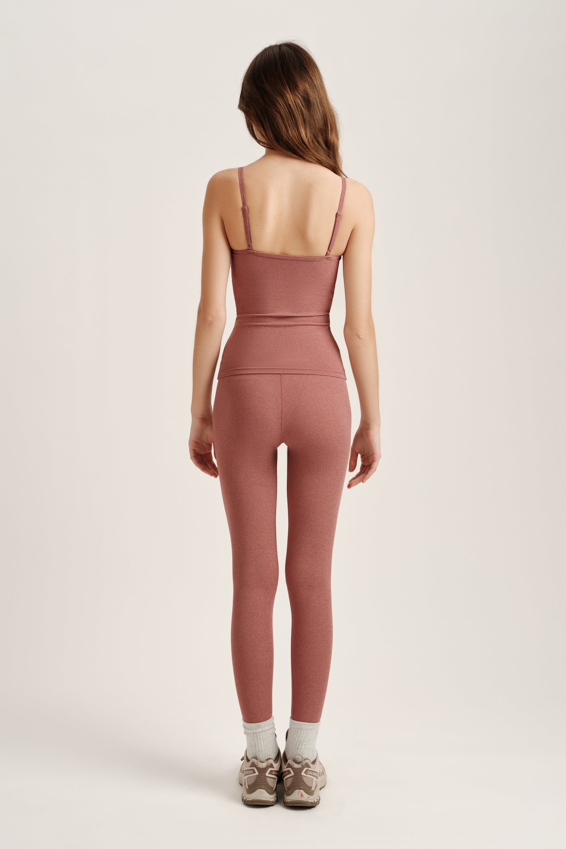 Person wearing a pink tank top and leggings on a white background