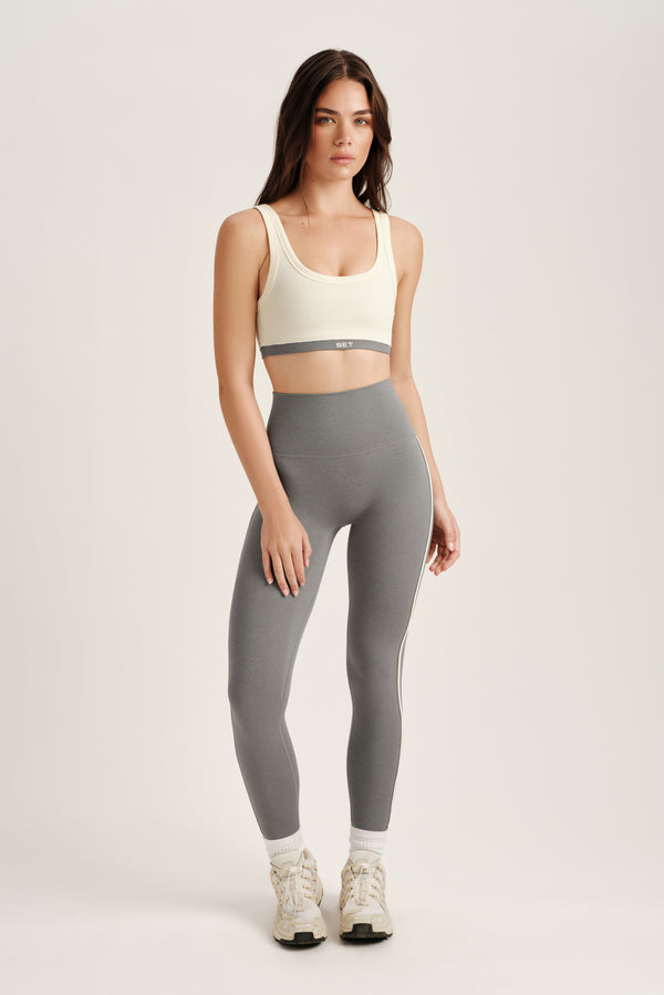 Woman wearing a white sports bra and gray leggings on a light background