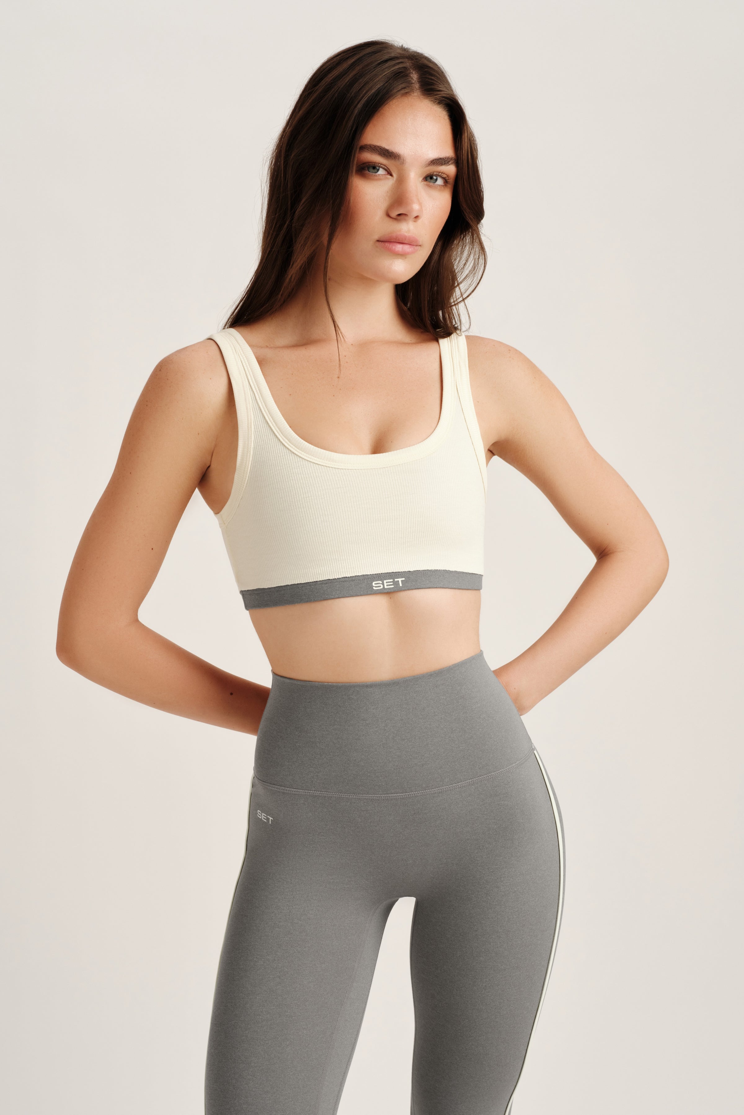 Woman wearing a white sports bra and gray leggings on a light background 