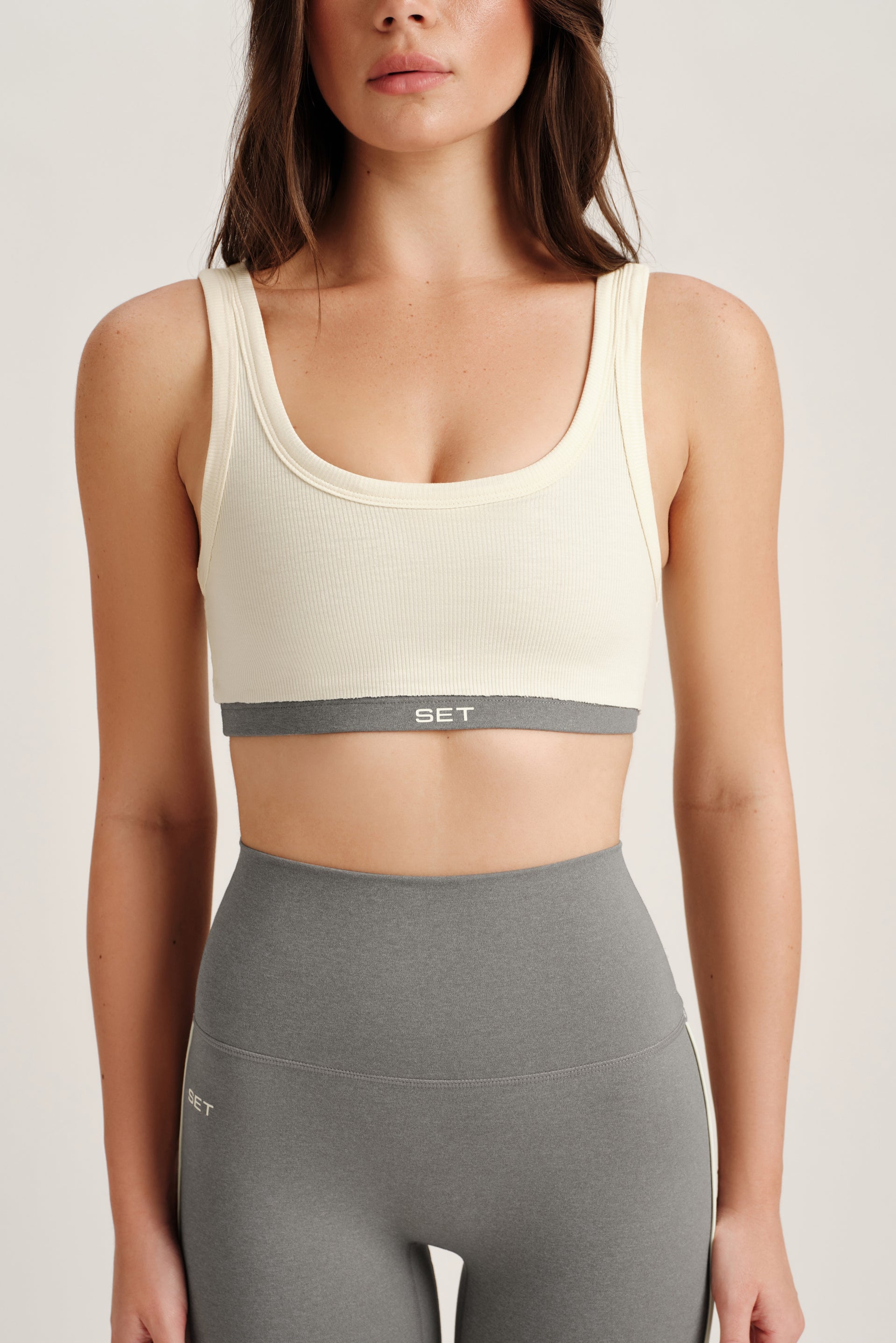 Woman wearing a beige sports bra and gray leggings on a plain background