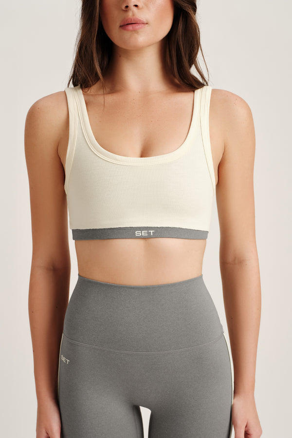 Woman wearing a beige sports bra and gray leggings on a plain background