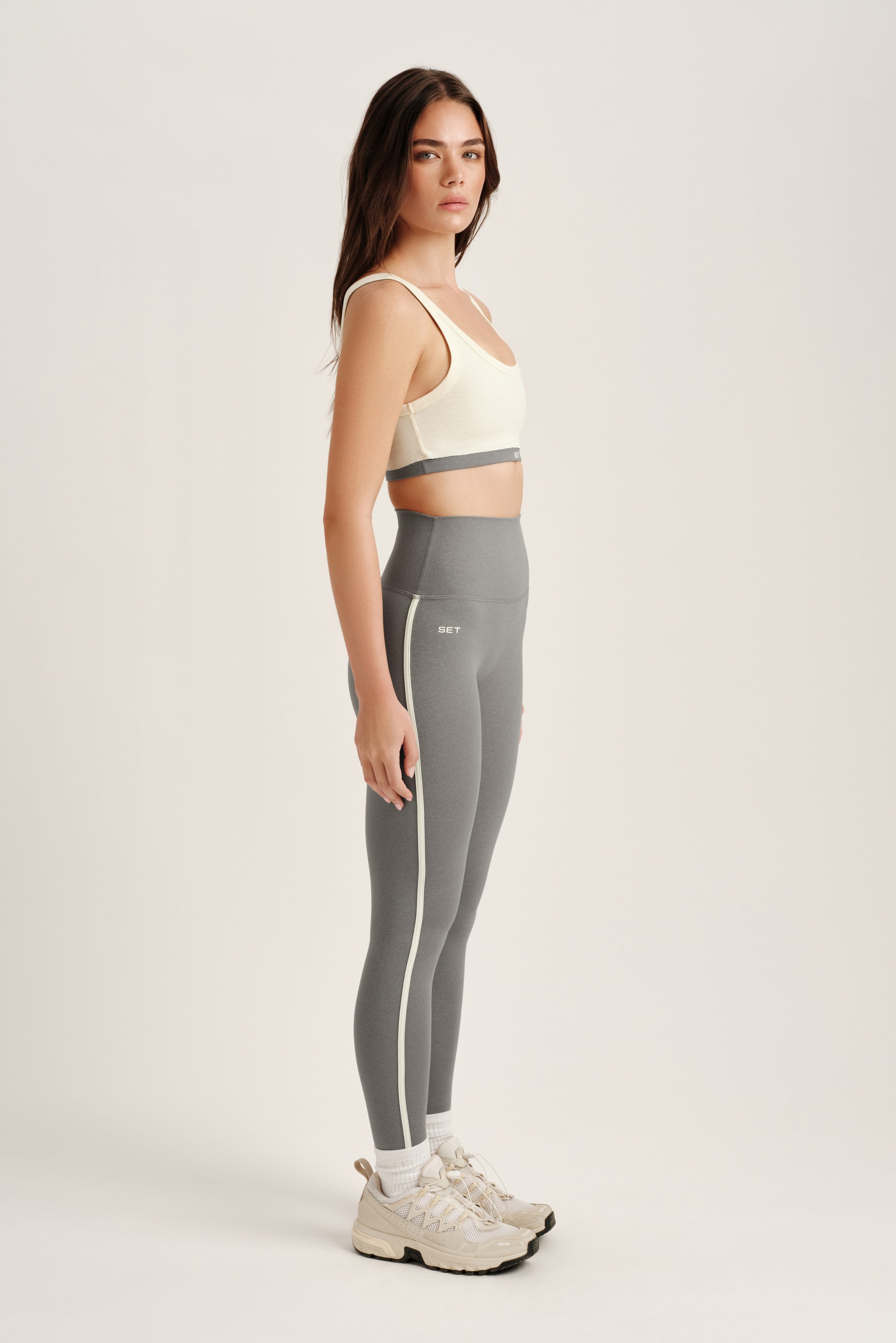 Woman wearing a sports bra and gray leggings on a white background