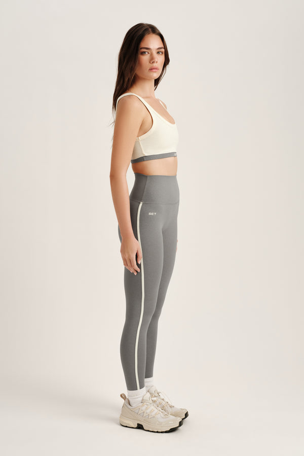 Woman wearing a sports bra and gray leggings on a white background