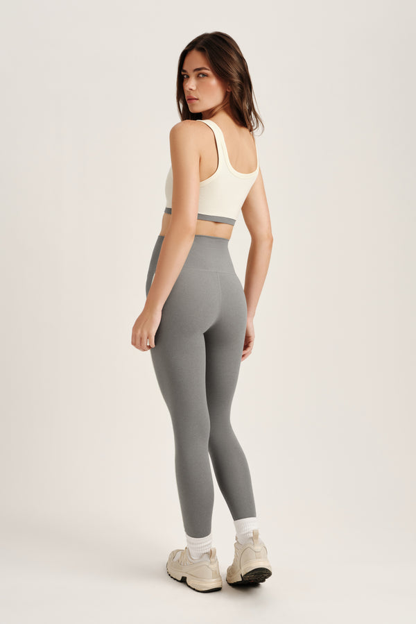 Woman wearing a white sports bra and gray leggings on a light gray background
