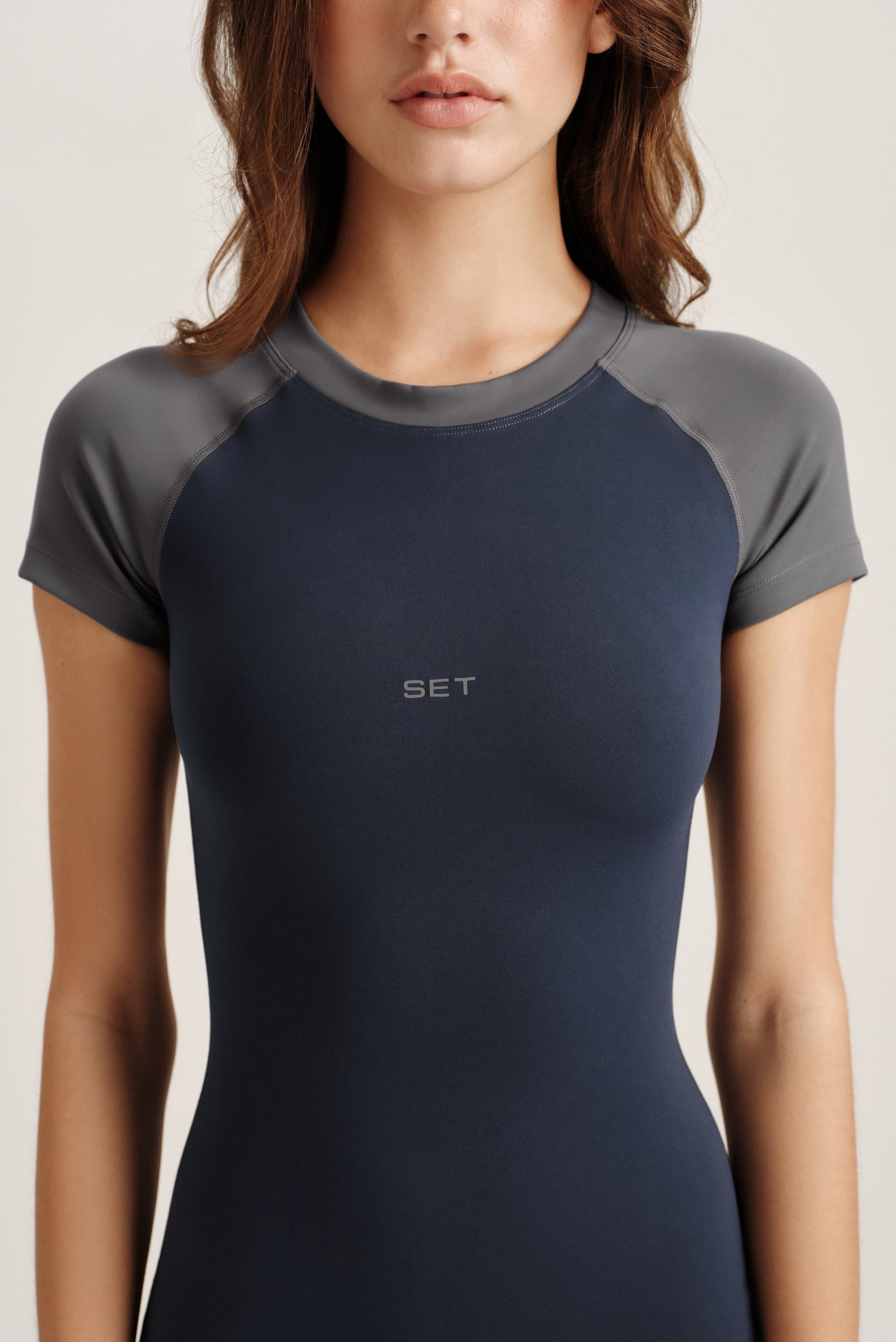 Woman wearing a dark blue athletic shirt with gray sleeves on a light background