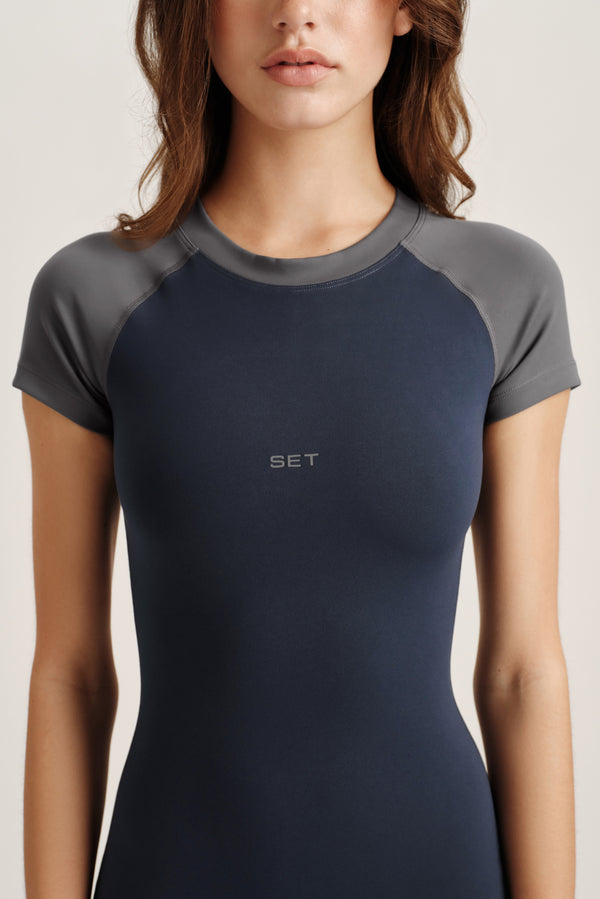 Woman wearing a dark blue athletic shirt with gray sleeves on a light background