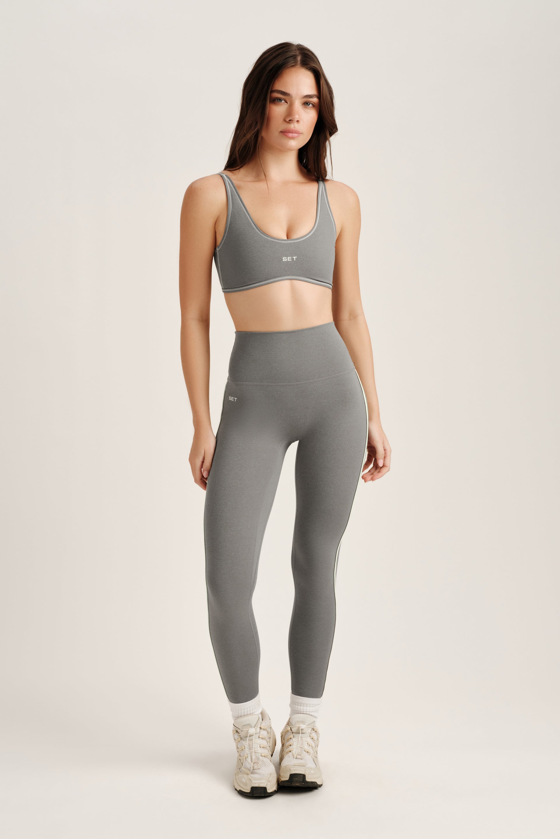 Woman wearing a gray sports bra and leggings set on a white background
