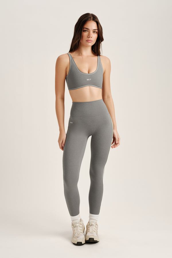Woman wearing a gray sports bra and leggings set on a white background