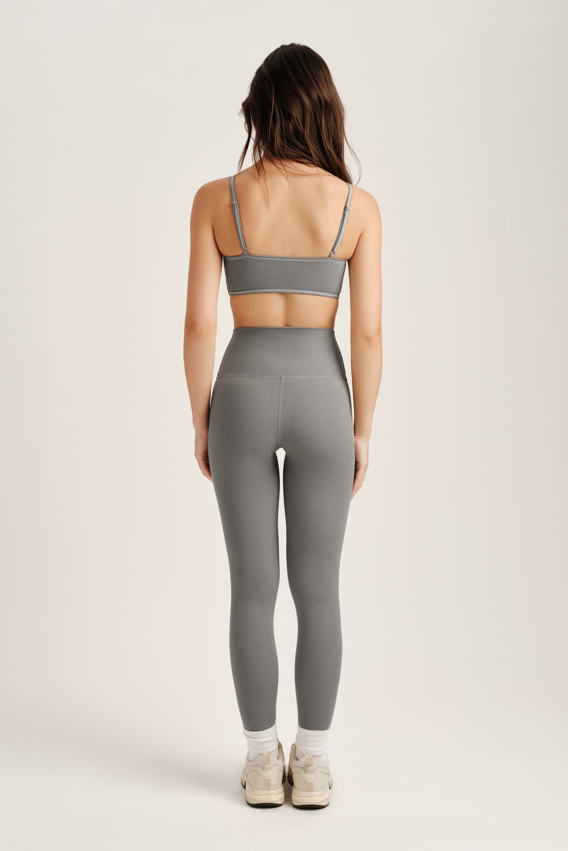 Person wearing a gray sports bra and leggings set on a white background