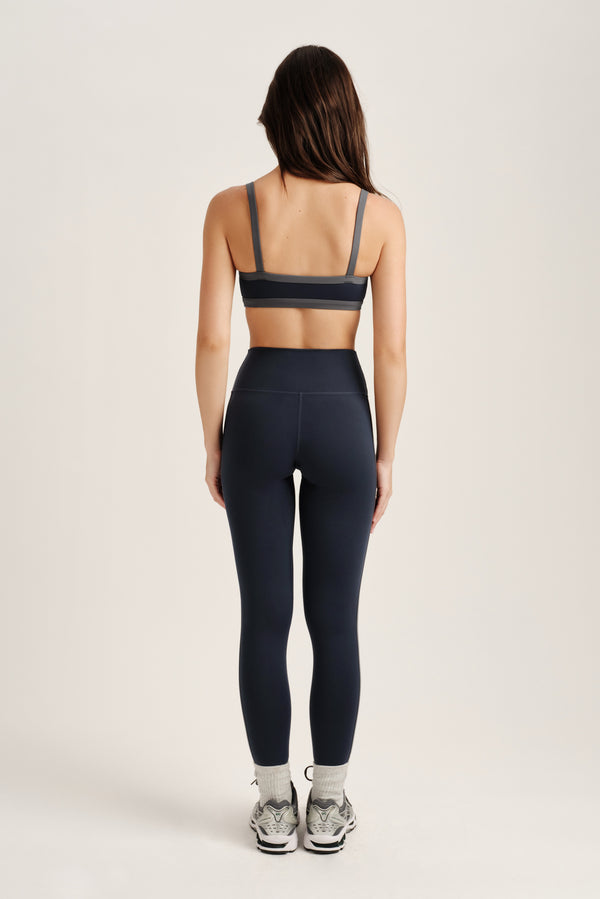 Person wearing a navy sports bra and leggings set on a light gray background