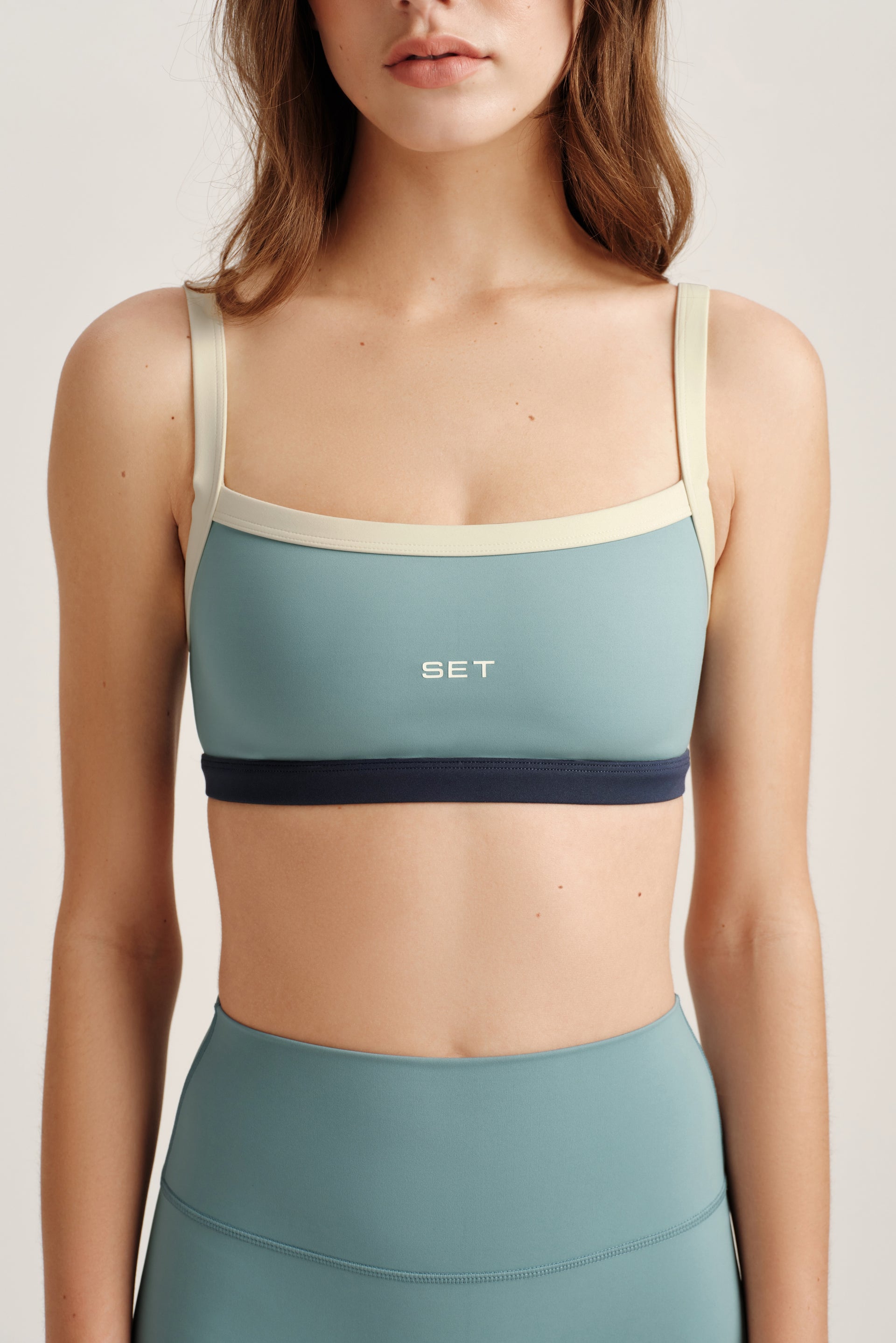 Woman wearing a teal sports bra and leggings with 'SET' branding on a light background