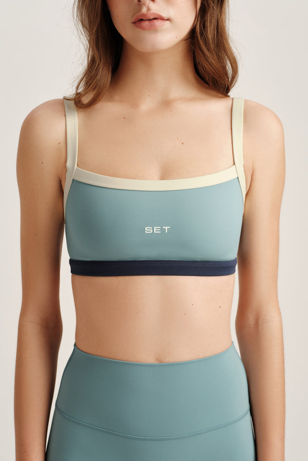 Woman wearing a teal sports bra and leggings with 'SET' branding on a light background