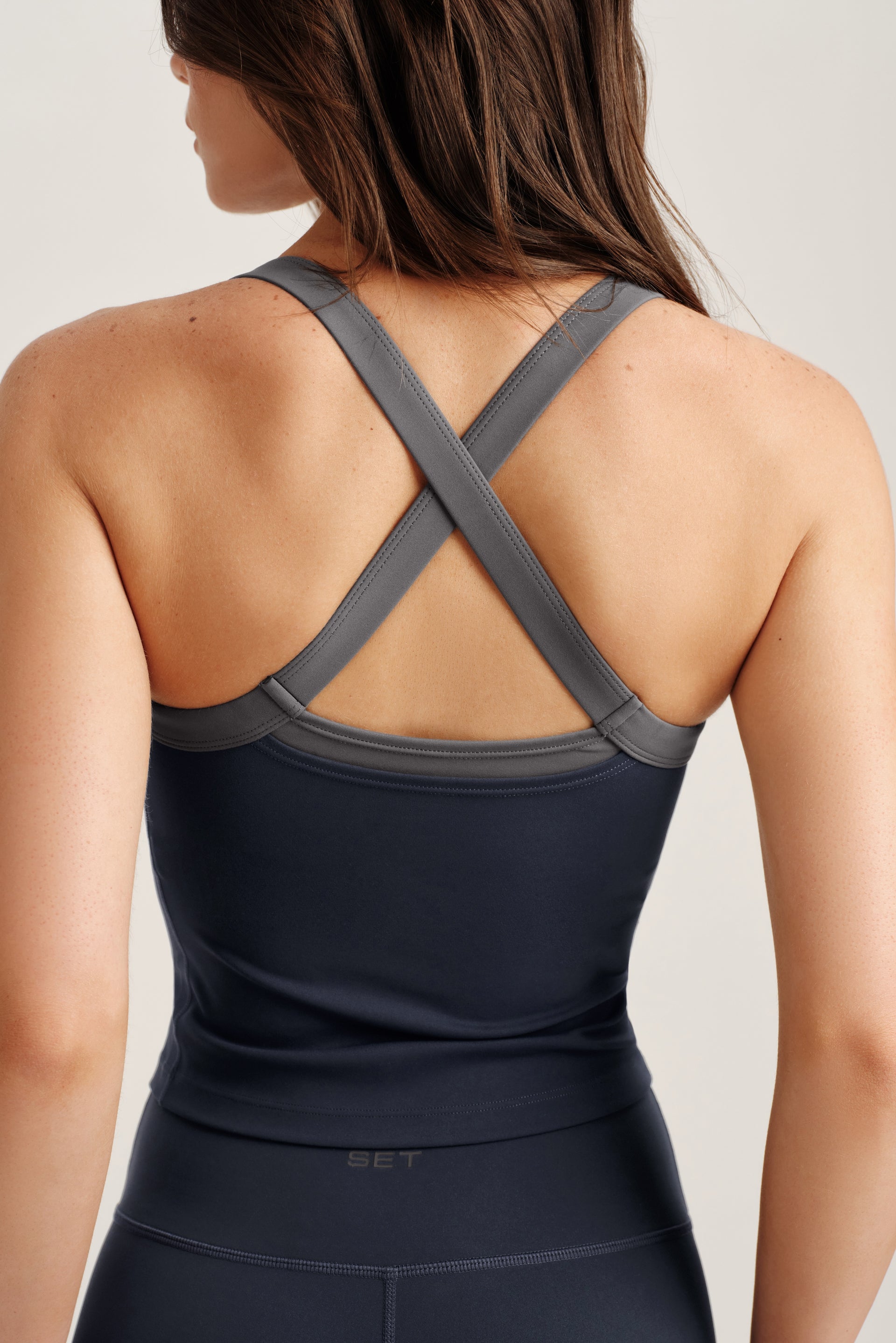 Person wearing a black athletic tank top with criss-cross straps on a light background