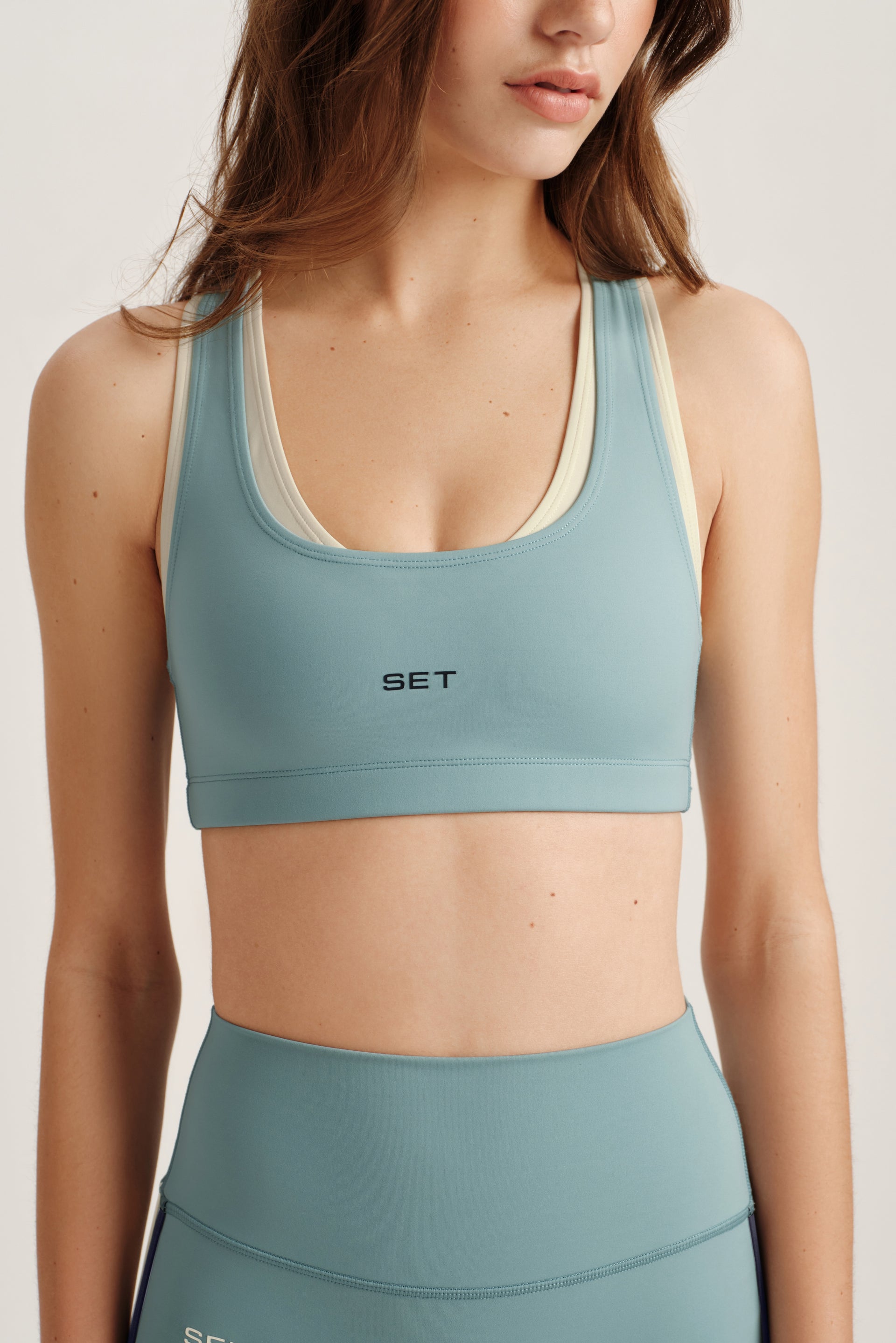 Woman wearing a teal sports bra and leggings with 'SET' branding on a light background