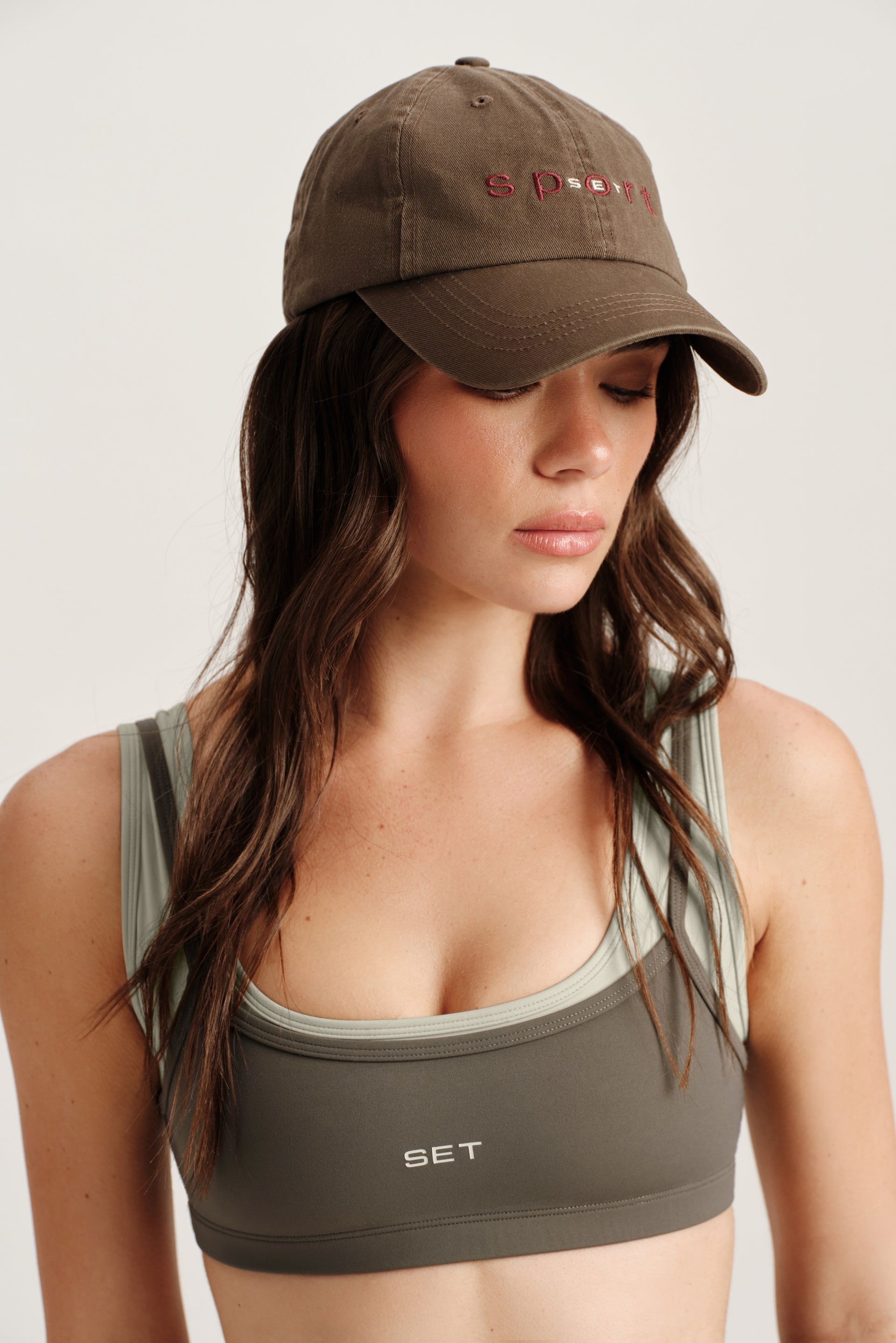 Woman wearing a green sports bra and cap with 'SET' branding on a plain background