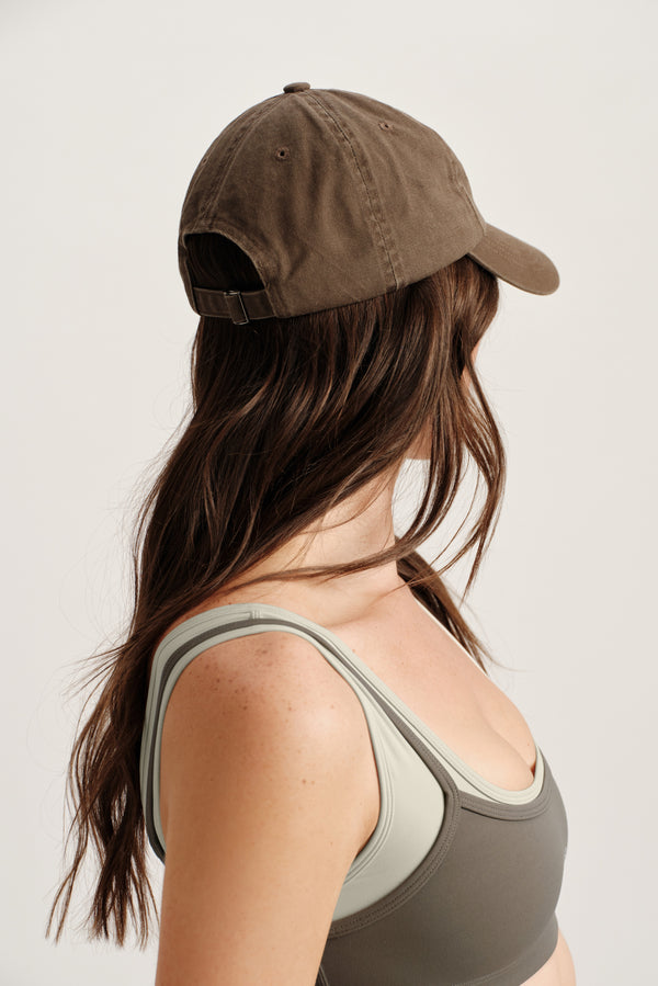 Woman wearing a brown cap and green tank top on a plain background