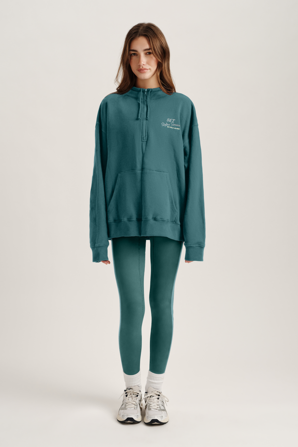 Woman wearing a teal hoodie and leggings set on a white background