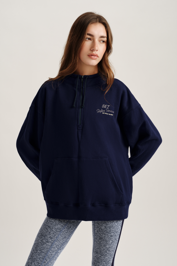 Person wearing a navy blue hoodie with a logo on a light gray background 