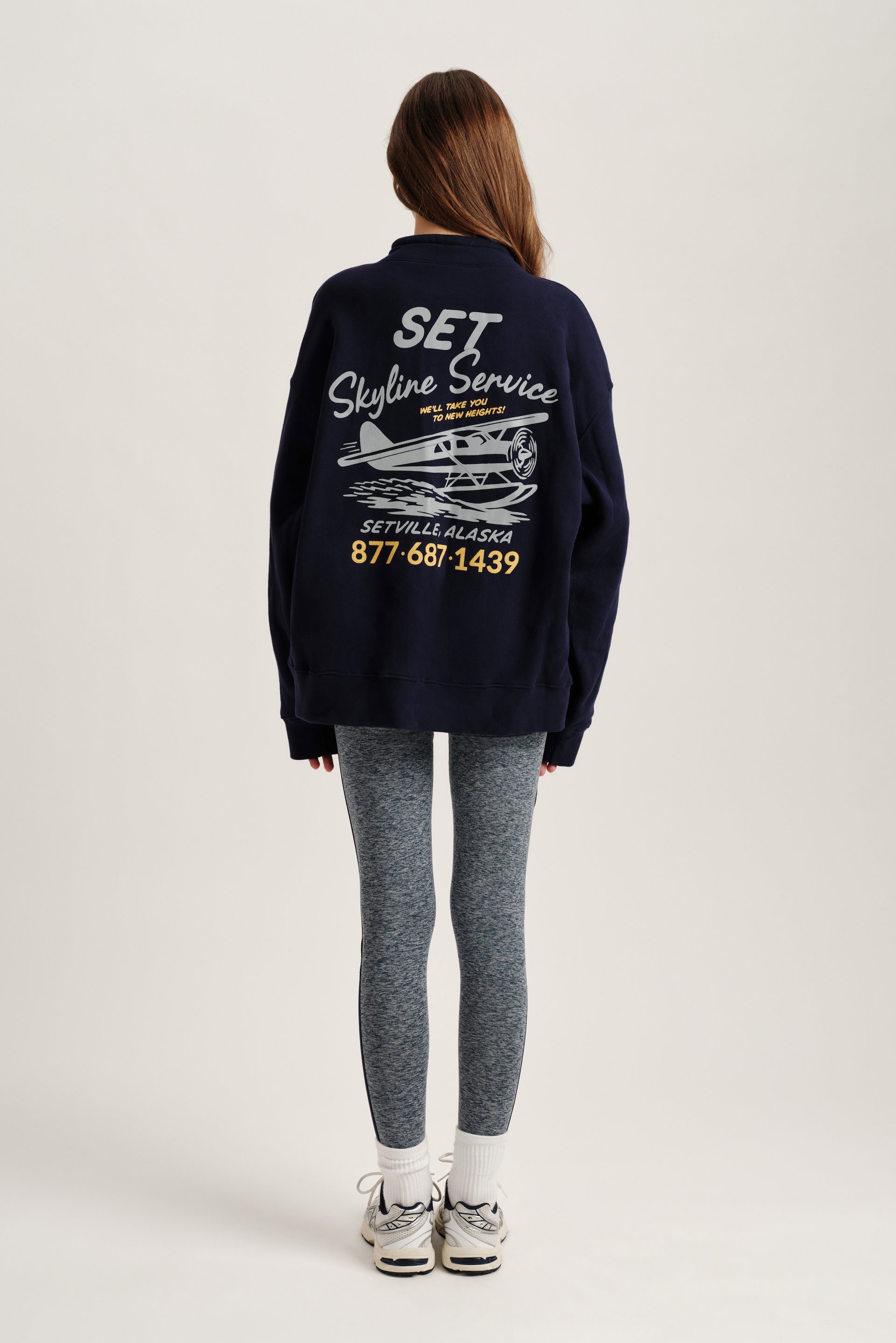 Person wearing a navy blue sweatshirt with graphics and text on the back, standing against a white background