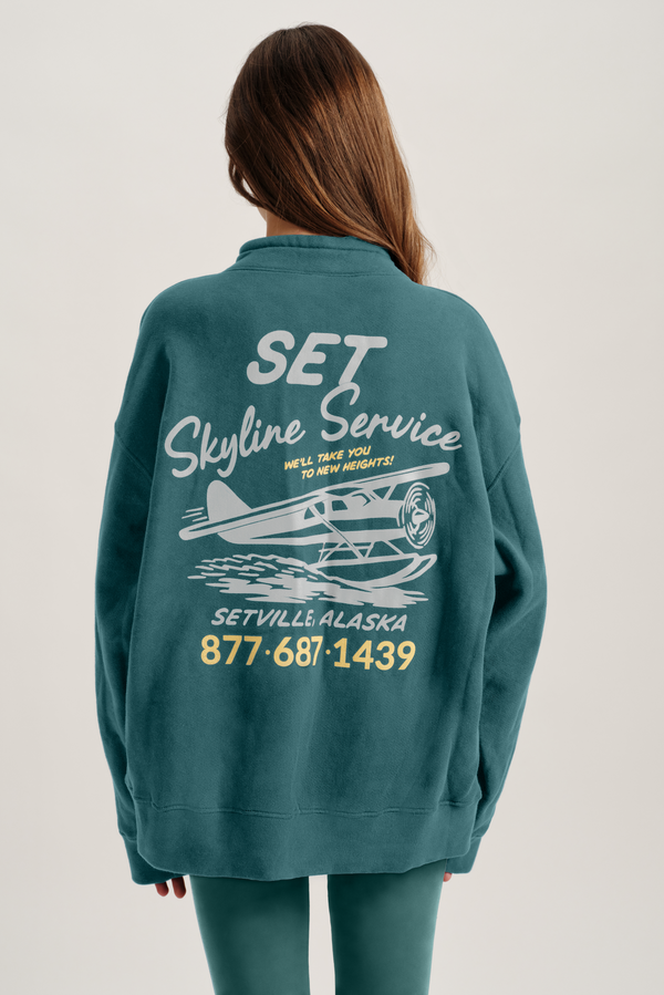 Person wearing a teal sweatshirt with 'Set Skyline Service' text and airplane graphic on the back.