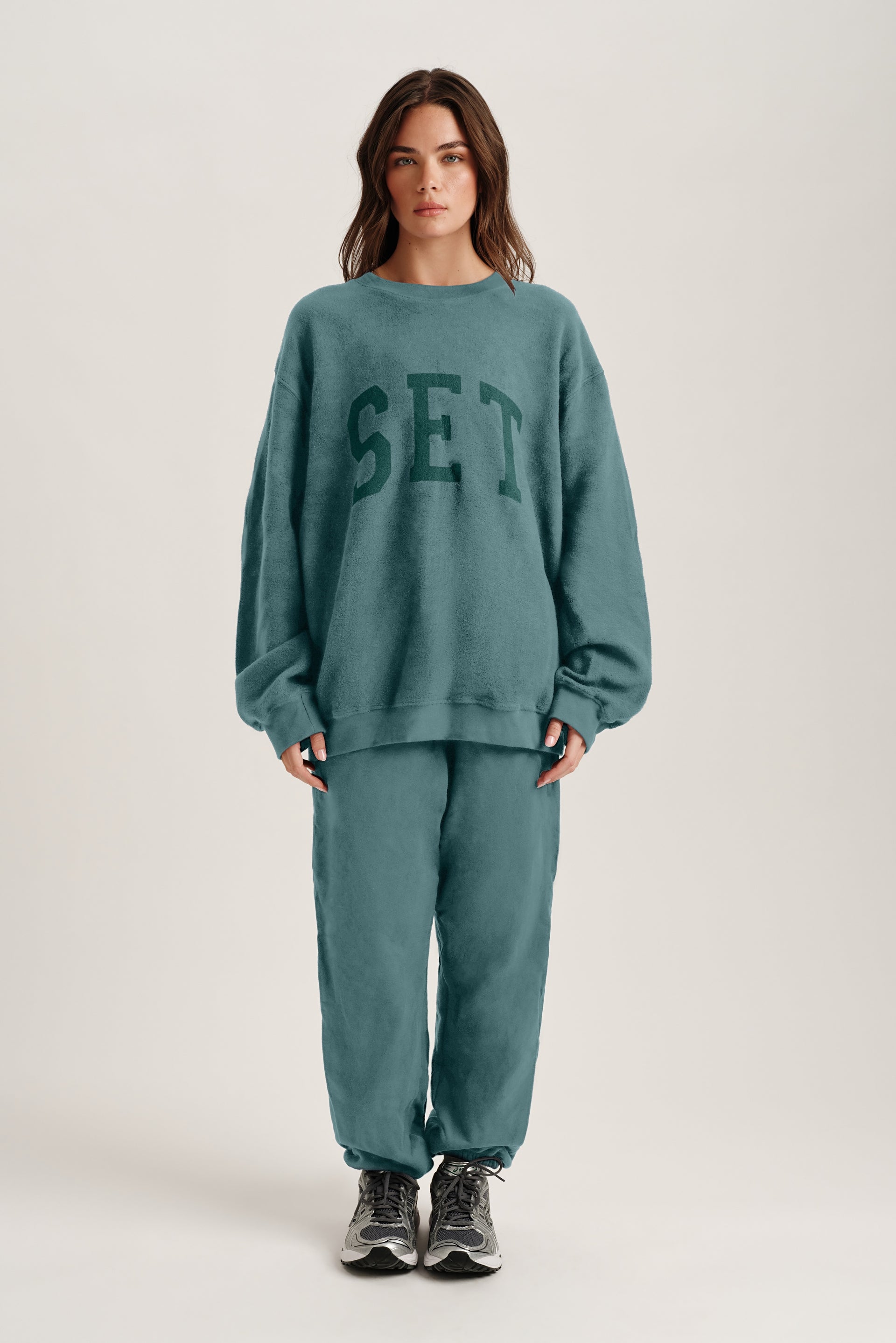 Person wearing a teal 'SET' sweatshirt and pants on a white background