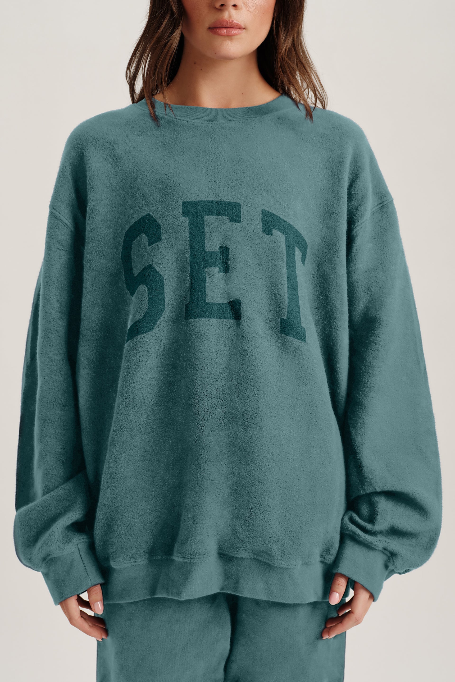 Person wearing a teal sweatshirt with 'SET' printed on it against a neutral background